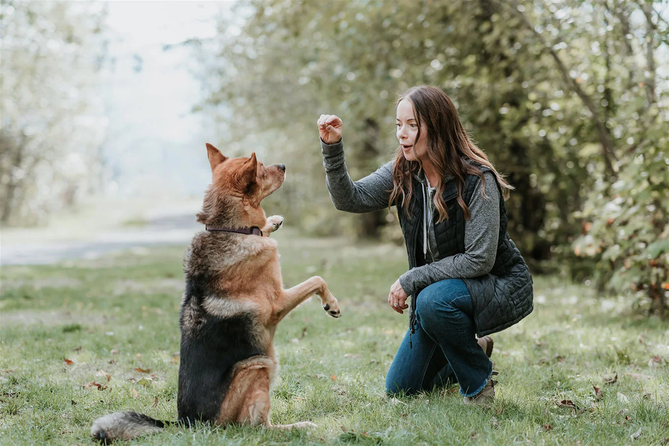 A woman crouching outdoors while training a German Shepherd dog.